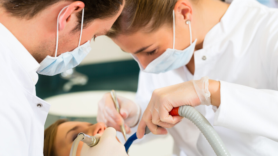 Eine Zahnmedizinische Fachangestellte (ZFA) assistiert dem Zahnarzt bei der Behandlung eines Patienten